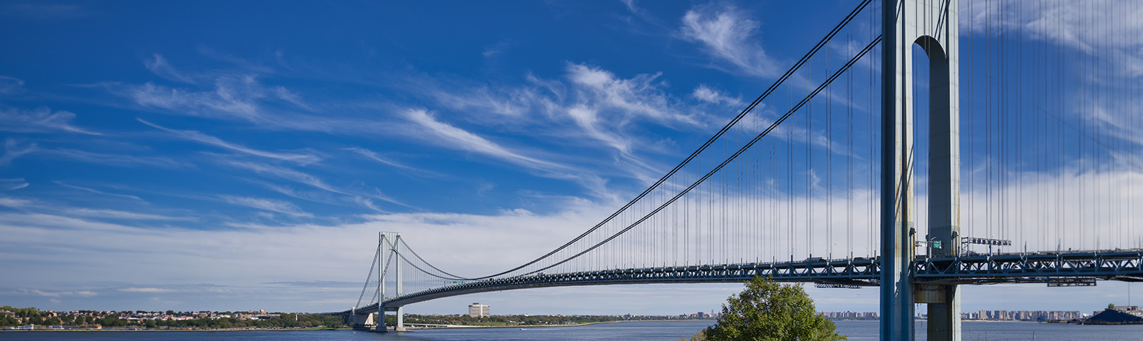The image displays a suspension bridge with a clear sky background, viewed from a distance across a body of water.
