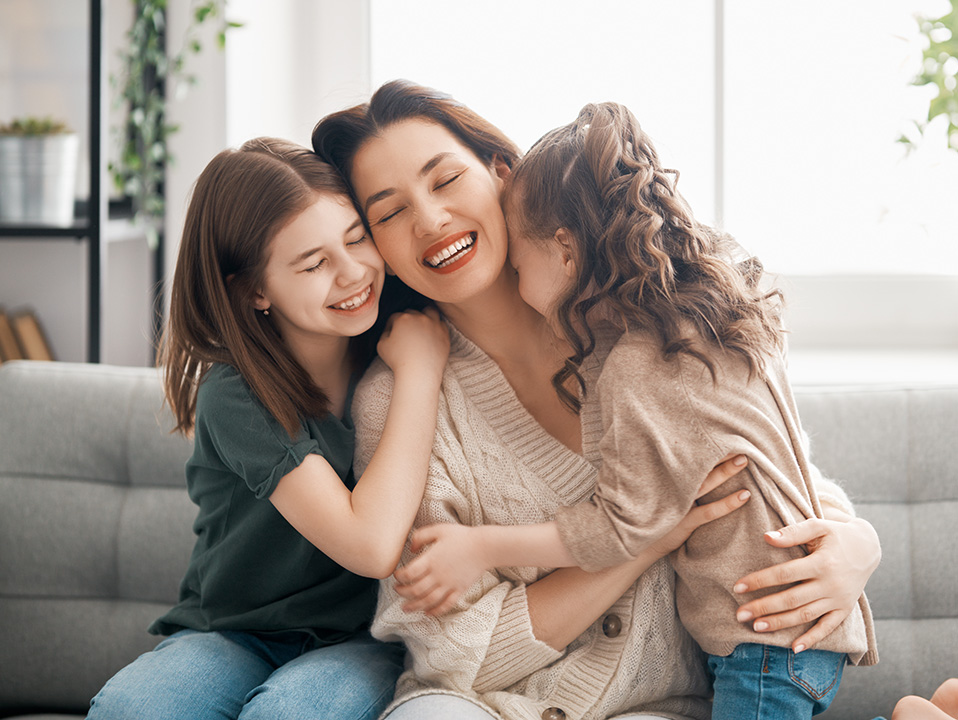 A woman hugging two children on a couch, all smiling and looking at the camera.